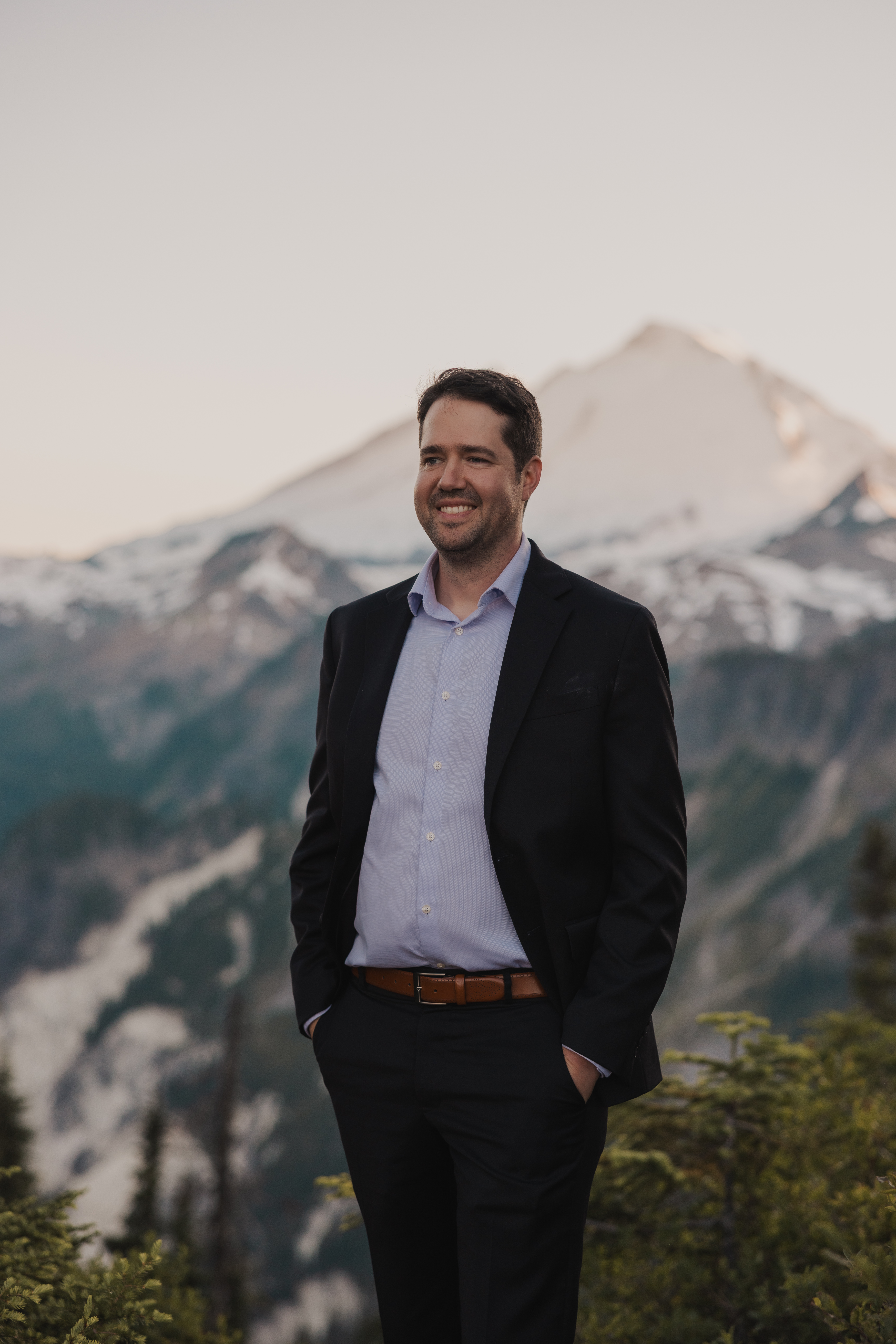 Lucas Ligon-Bruno standing in front of Mount Baker at dusk, smiling, in a charcoal suit